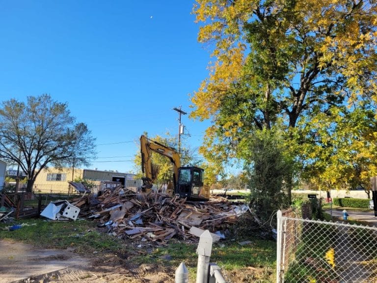 Excavator knocking an older house down to a debris pile for a house and garage teardown near El Camino Real