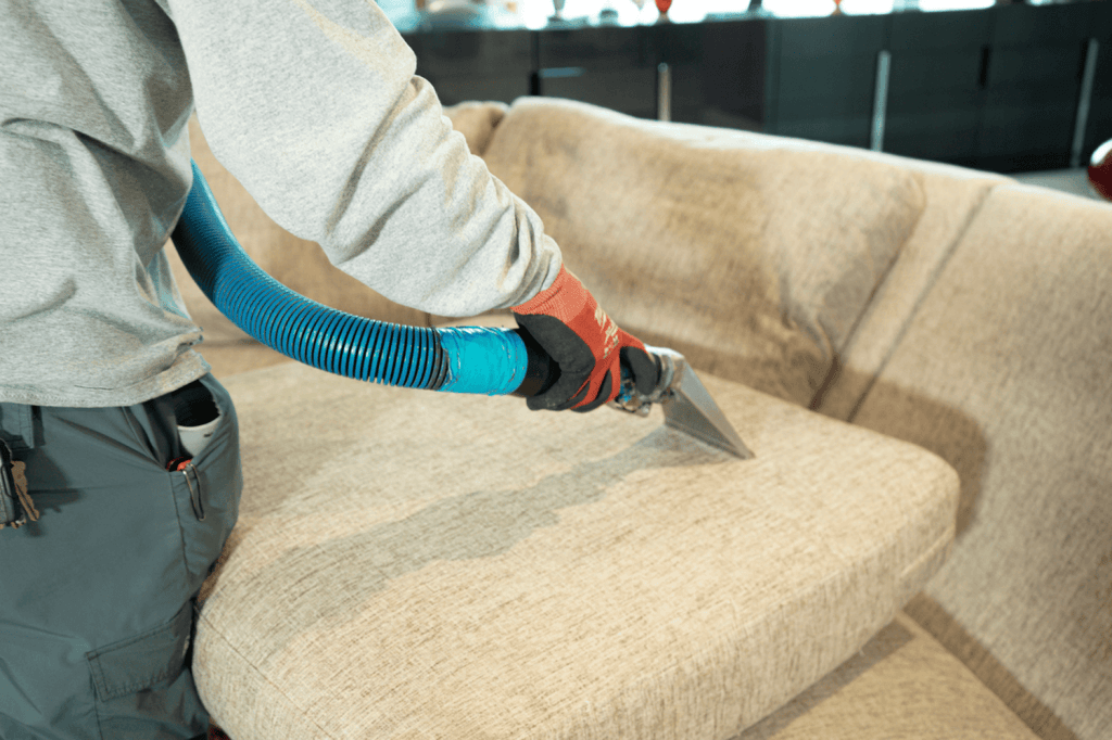 Person using upholstery cleaning equipment on a beige sofa, demonstrating professional cleaning techniques for furniture restoration.