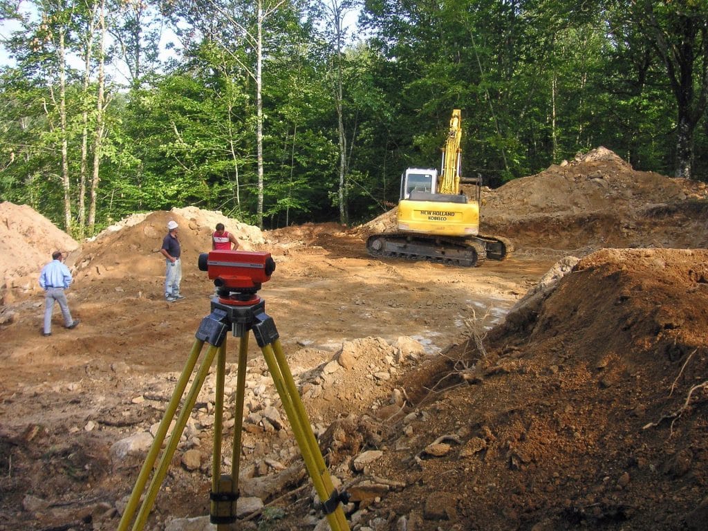 Construction site with surveying equipment, excavator, and workers assessing land preparation for excavation and grading in Houston.