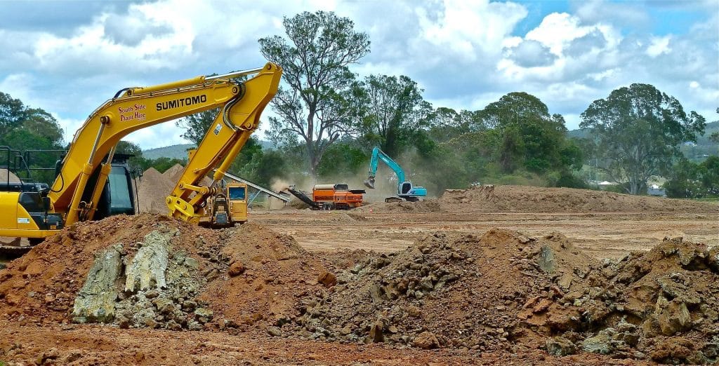 Excavators and bulldozer on a land clearing site in Houston, TX, preparing ground for construction with debris and mounds of dirt visible.