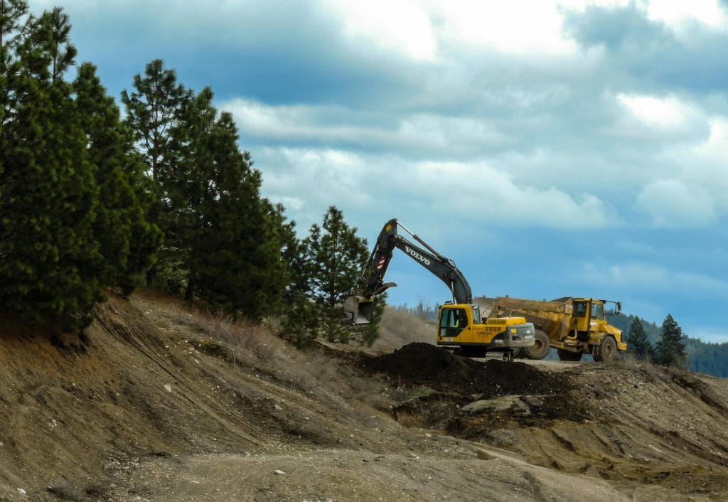 Excavator and dump truck on construction site clearing land, surrounded by trees, emphasizing site preparation for future development in Houston, TX.