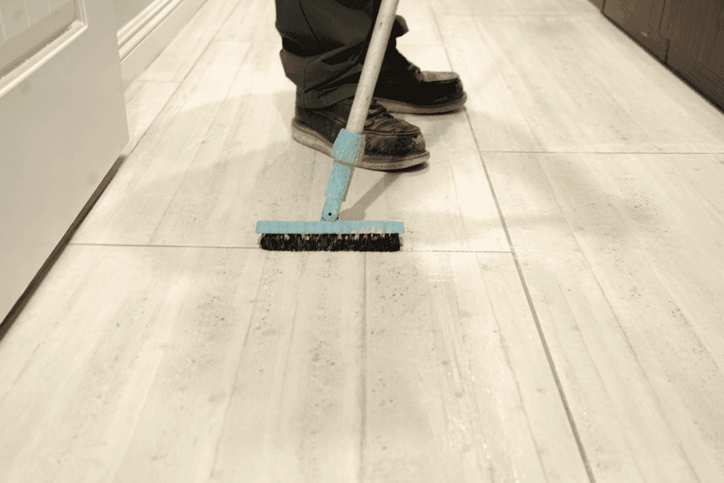 Person cleaning tile floor with a brush, showcasing professional tile and grout cleaning services for a spotless environment.
