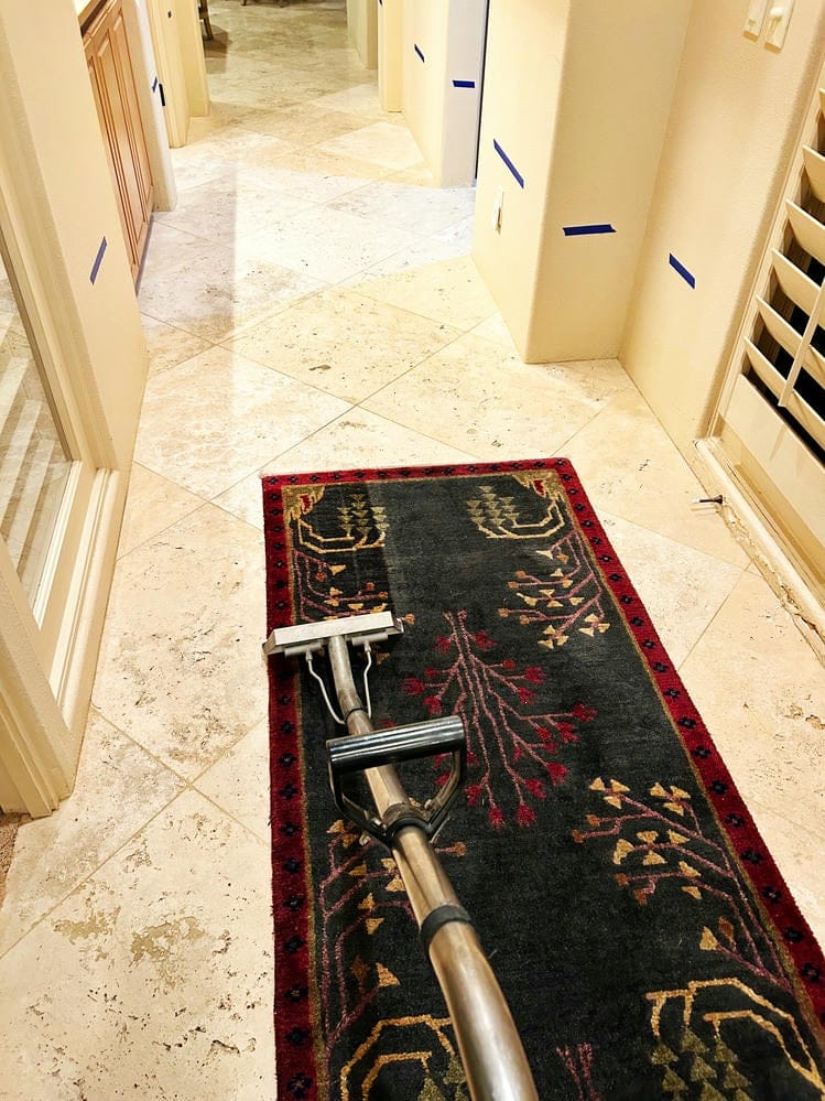 Vacuum cleaning a patterned area rug in a well-lit hallway with tiled flooring, illustrating VM Demolition's thorough cleaning services.